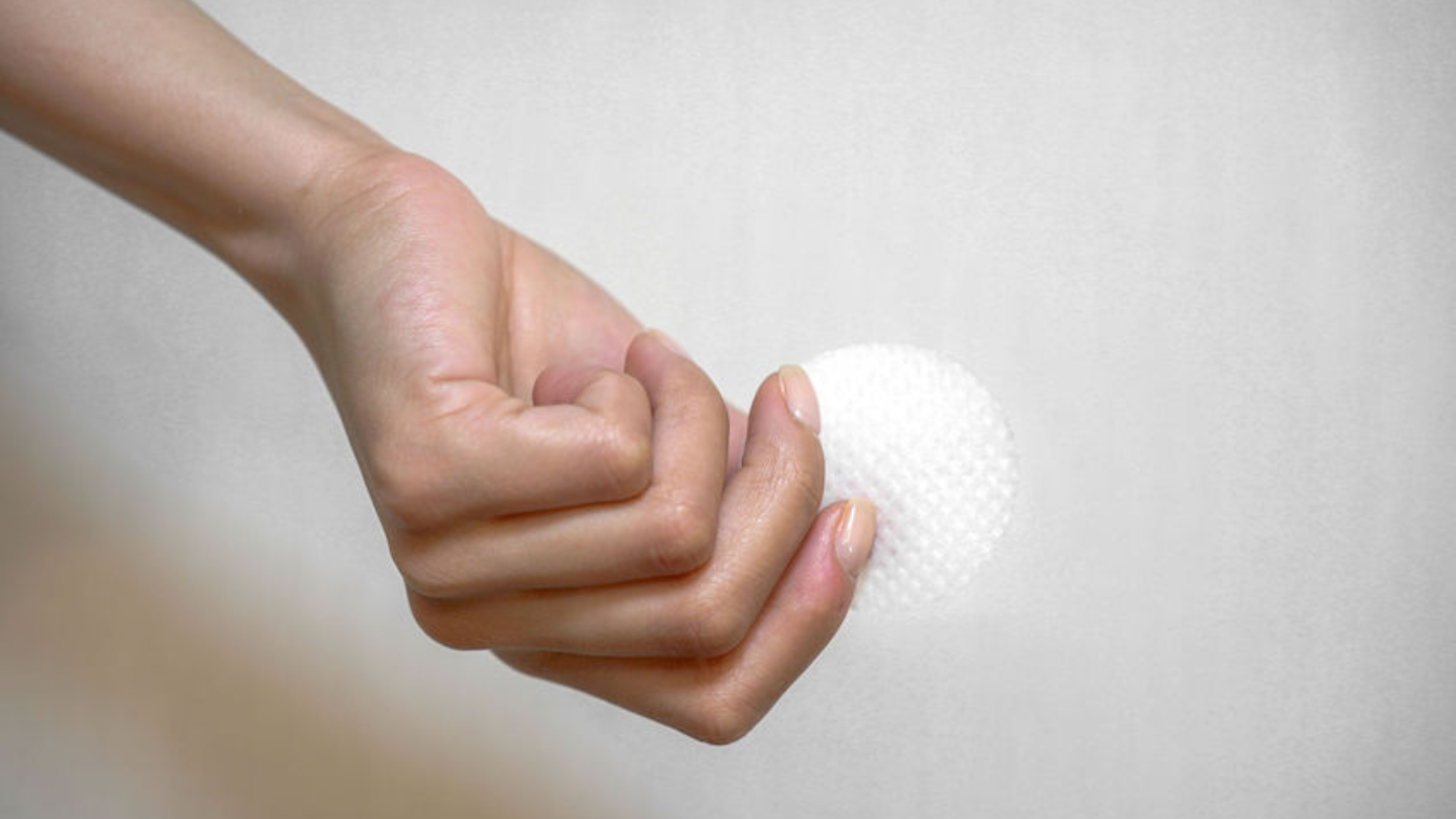 Skincare mistakes blog image. Hand holding out a cotton swab on a white background