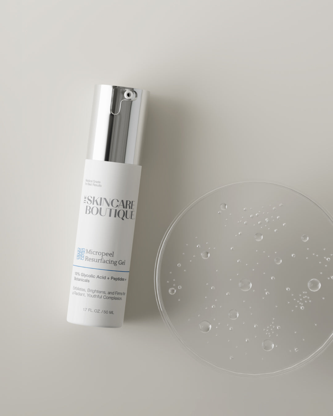 A skincare pump bottle labeled 'SKINCARE BOUTIQUE' with a reflective silver cap, placed beside a clear circular dish with water droplets on a light gray background.
