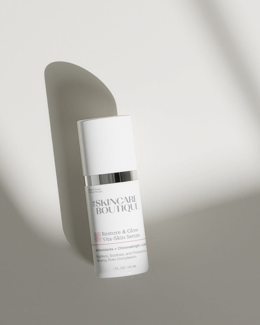 A white skincare bottle with a silver band and black text reading 'SKINCARE BOUTIQUE Restore & Glow Vita-Skin Serum' on a light gray background with soft diagonal shadows.
