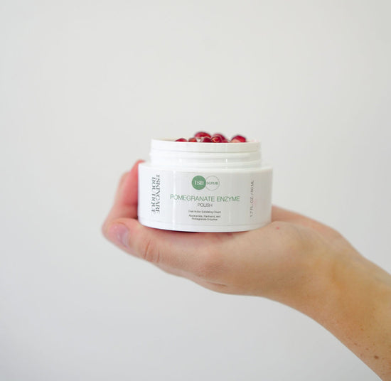 POMEGRANATE ENZYME POLISH BEING HELD IN HAND WITH POMEGRANATES SITTING ON TOP