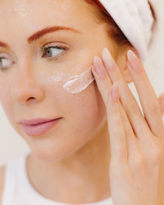 Woman applying cream to her face with a towel on her head