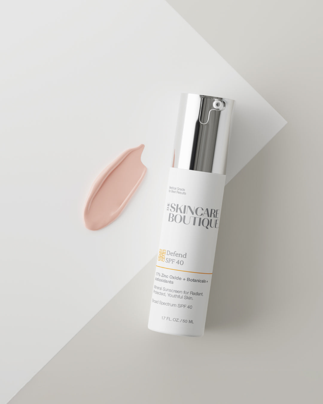 A skincare bottle with a silver pump and white label, placed diagonally on a light gray surface with a peach-colored cosmetic smear beside it. The label shows the brand SKINCARE BOUTIQUE and SPF 40 text.